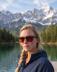 Woman, 27, wearing Peppers Beachcomber sunglasses in Matte Black Frame with Brown Fire Red Mirror Lens, on a mountain lake dock