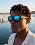 Man, 27, wearing Peppers Big Kahuna sunglasses in Matte Black Frame with Blue Mirror Lens, at a calm bay beach