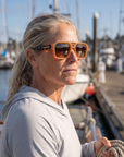 Woman, 45, wearing Peppers Cascade sunglasses in Caramel Frame / Tort Temples with Brown Lens, on a charter boat deck in a fishing harbour