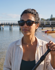 Woman, 29, wearing Peppers Chilmark sunglasses in Shiny Black to Tort Frame with Smoke Lens, at a calm bay