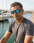 Man, 43, wearing Peppers Cutthroat sunglasses in Matte Black Frame with Brown Ice Blue Mirror Lens, on a waterfront bike path along a harbour