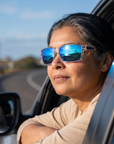 Woman, 48, wearing Peppers Gambler sunglasses in Crystal Clear Frame with Blue Diamond Mirror Lens, on a seaside road