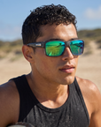 Man, 24, wearing Peppers Gambler sunglasses in Grey Woody Demi Frame with Brown Emerald Green Mirror Lens, at a surf beach