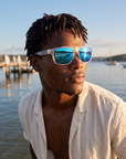 Man, 27, wearing Peppers Grand Teton sunglasses in Matte Crystal Frame with Blue Revo Lens, at a calm bay beach
