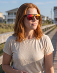 Woman, 31, wearing Peppers Grand Teton sunglasses in Matte Black Frame with Red Mirror Lens, on a beach boardwalk