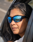 Woman, 48, wearing Peppers Grand Slam sunglasses in Crystal Blue Frame with Blue Revo Lens, on a seaside road