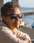 Woman, 53, wearing Peppers Grand Slam sunglasses in Matte Black Frame with Smoke Lens, on a porch overlooking a harbour