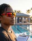 Woman, 34, wearing Peppers Grand Slam sunglasses in Matte Black Frame with Red Revo Lens, on an ocean-side pool deck