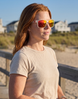Woman, 31, wearing Peppers Islander sunglasses in Matte Frosted White Frame with Red Diamond Mirror Lens, on a beach boardwalk