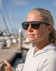 Woman, 45, wearing Peppers Milano sunglasses in Shiny Black to Shiny Tort Frame with G15 Lens, on a charter boat deck in a fishing harbour