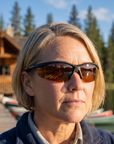 Woman, 43, wearing Peppers Ricochet sunglasses in Matte Black Frame with Brown Lens, at a mountain-lake lodge dock