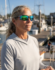 Woman, 45, wearing Peppers Ricochet sunglasses in Matte Dark Green / Silver Frame with Green Diamond Mirror Lens, on a charter boat deck in a fishing harbour