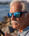 Man, 61, wearing Peppers Sea Dweller 2.0 sunglasses in Matte Black Frame with Blue Revo Lens, on a river-mouth jetty