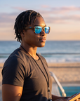 Woman, 34, wearing Peppers Seawitch sunglasses in Matte Black to Tort Frame with Blue Revo Lens, on an ocean-side pool deck