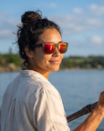 Woman, 29, wearing Peppers Sweetwater sunglasses in Matte Black Frame with Red Mirror Lens, on a calm bay