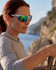 Woman, 35, wearing Peppers Three Wood sunglasses in Matte White Frame with Green Revo PC Lens, on a sea cliff