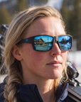 Woman, 27, wearing Peppers Whaler sunglasses in Matte Black Frame with Blue Diamond Mirror Lens, at the base of a ski area
