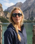 Woman, 27, wearing Peppers Big Kahuna sunglasses in Matte Black Frame with Smoke Lens, on a mountain lake dock