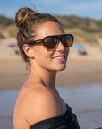 Woman, 23, wearing Peppers Cascade sunglasses in Black to Transparent Yellow Frame with Tea Lens, on a surf beach