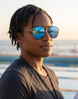 Woman, 34, wearing Peppers Django sunglasses in Shiny Dark Antique Silver Frame with Blue Mirror Lens, on an ocean-side pool deck