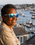 Woman, 53, wearing Peppers Hammerhead sunglasses in Metallic Silver Frame with Blue Revo Mirror Lens, on a porch overlooking a harbour