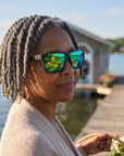 Woman, 59, wearing Peppers Hammerhead sunglasses in Matte Dark Grey Frame with Green Revo Lens, on a lakeside garden dock