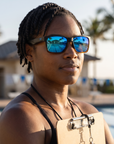Woman, 34, wearing Peppers Islander sunglasses in Matte Black to Tort Frame with Blue Diamond Mirror Lens, on an ocean-side pool deck