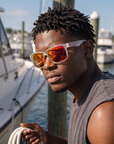 Man, 26, wearing Peppers Islander sunglasses in Matte Frosted White Frame with Red Diamond Mirror Lens, at a busy marina