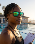 Woman, 34, wearing Peppers Low Rider sunglasses in Matte Black Frame with Green Revo Lens, on an ocean-side pool deck