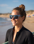 Woman, 23, wearing Peppers Mountain Madness sunglasses in Matte Crystal Blue to Black Frame with Blue Diamond Mirror Lens, on a surf beach