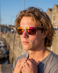 Man, 22, wearing Peppers Mountain Madness sunglasses in Matte Crystal Clear to Black Fade Frame with Red Diamond Mirror Lens, at a harbour skate spot