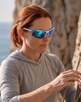 Woman, 35, wearing Peppers Ricochet sunglasses in Matte White / Blue Frame with Blue Diamond Mirror Lens, on a sea cliff