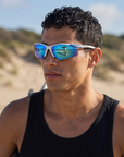 Man, 24, wearing Peppers Ricochet sunglasses in Matte White / Blue Frame with Blue Diamond Mirror Lens, at a surf beach