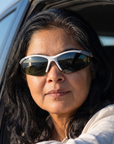 Woman, 48, wearing Peppers Ricochet sunglasses in Matte White / Silver Frame with G15 Lens, on a seaside road