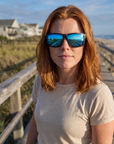 Woman, 31, wearing Peppers Sea Dweller 2.0 sunglasses in Matte Black Frame with Blue Revo Lens, on a beach boardwalk