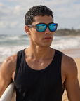 Man, 24, wearing Peppers Sweetwater sunglasses in Shiny Demi Frame with Blue Mirror Lens, on a surf beach after a session